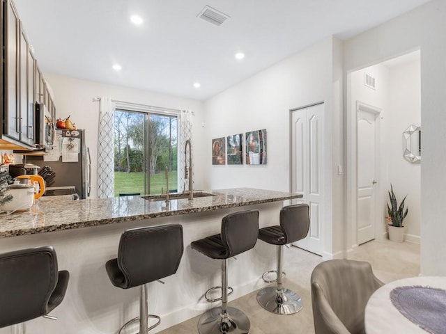 kitchen featuring kitchen peninsula, light stone countertops, a breakfast bar, and sink