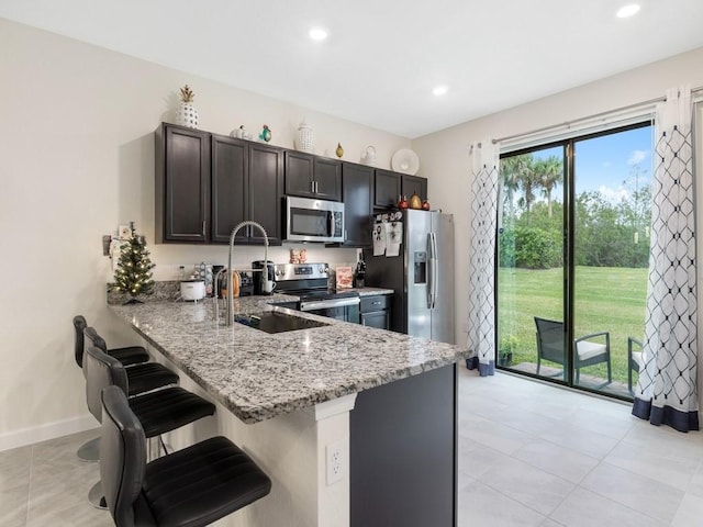 kitchen with a kitchen breakfast bar, appliances with stainless steel finishes, light stone countertops, kitchen peninsula, and sink