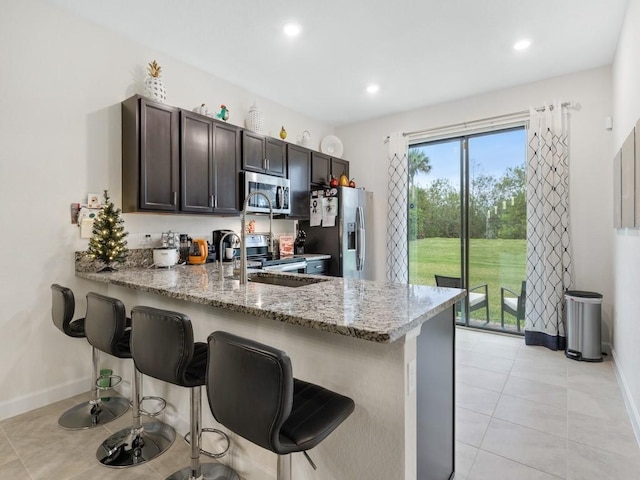 kitchen featuring stainless steel appliances, light stone countertops, kitchen peninsula, a kitchen bar, and dark brown cabinets