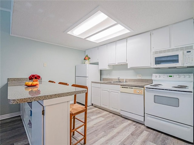 kitchen with a breakfast bar area, white cabinets, white appliances, and light wood-style floors