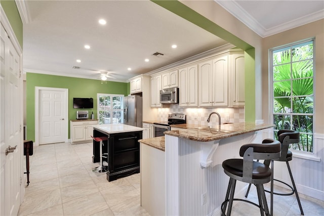 kitchen with a center island, appliances with stainless steel finishes, a kitchen breakfast bar, kitchen peninsula, and light stone countertops