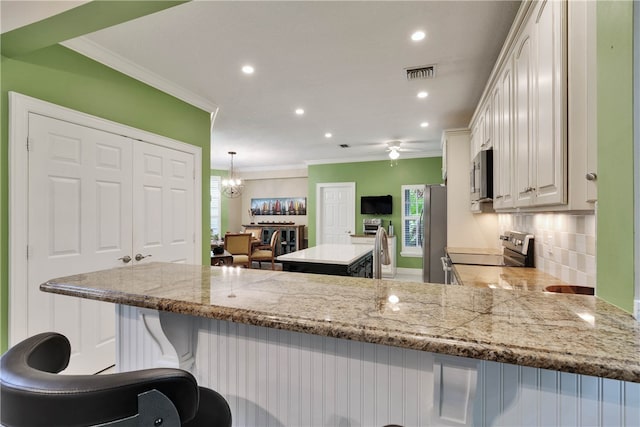 kitchen with a breakfast bar, appliances with stainless steel finishes, hanging light fixtures, white cabinets, and kitchen peninsula