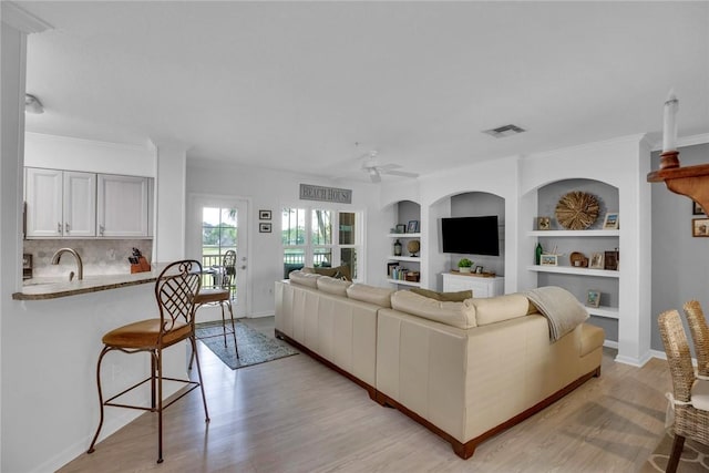 living area featuring light wood-type flooring, ceiling fan, visible vents, and crown molding