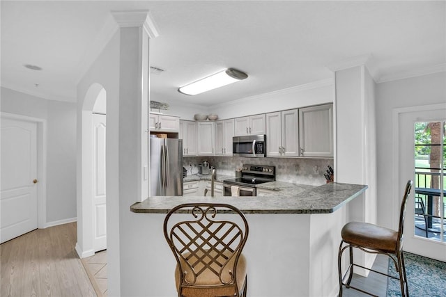 kitchen with arched walkways, a peninsula, a kitchen breakfast bar, appliances with stainless steel finishes, and tasteful backsplash