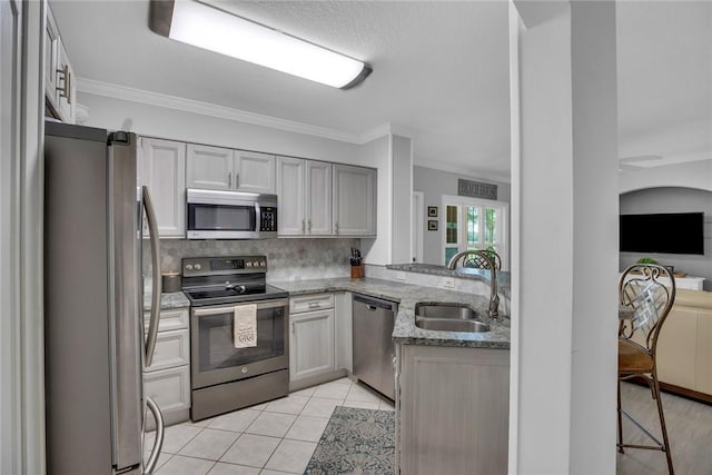 kitchen with decorative backsplash, appliances with stainless steel finishes, light tile patterned flooring, a sink, and light stone countertops