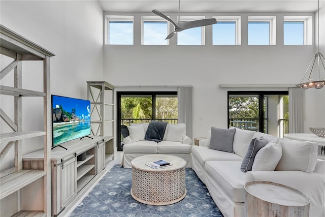 living room featuring ceiling fan with notable chandelier, a healthy amount of sunlight, and a high ceiling