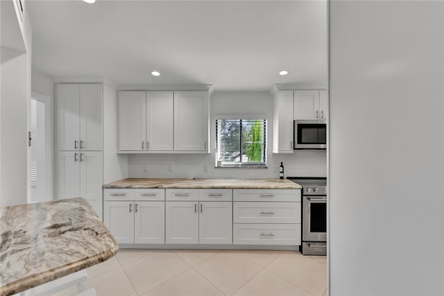 kitchen with stainless steel appliances, white cabinets, decorative backsplash, light tile patterned floors, and light stone countertops