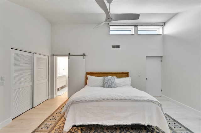 bedroom featuring light hardwood / wood-style floors, a barn door, ensuite bathroom, ceiling fan, and a closet