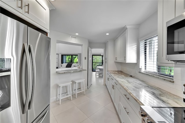 kitchen featuring white cabinetry, appliances with stainless steel finishes, a healthy amount of sunlight, and light stone counters