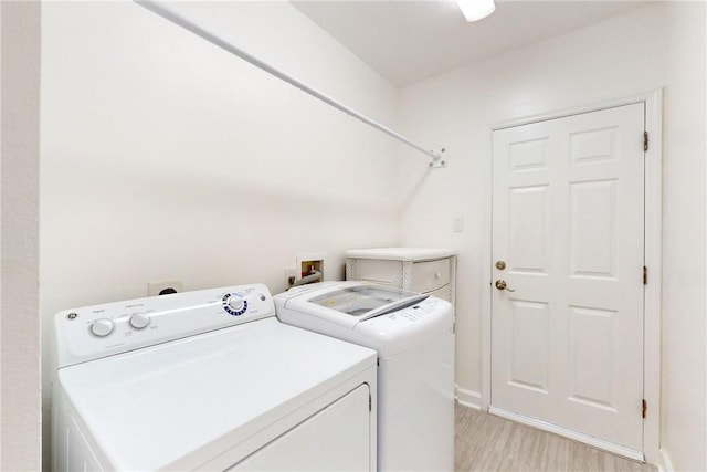clothes washing area featuring light wood-type flooring, separate washer and dryer, laundry area, and baseboards