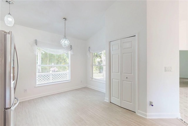 unfurnished dining area featuring baseboards, an inviting chandelier, light wood finished floors, and vaulted ceiling