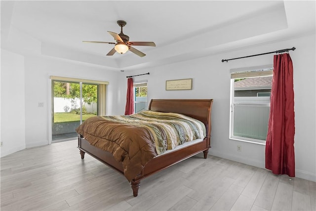 bedroom featuring a raised ceiling, access to exterior, ceiling fan, and light hardwood / wood-style flooring