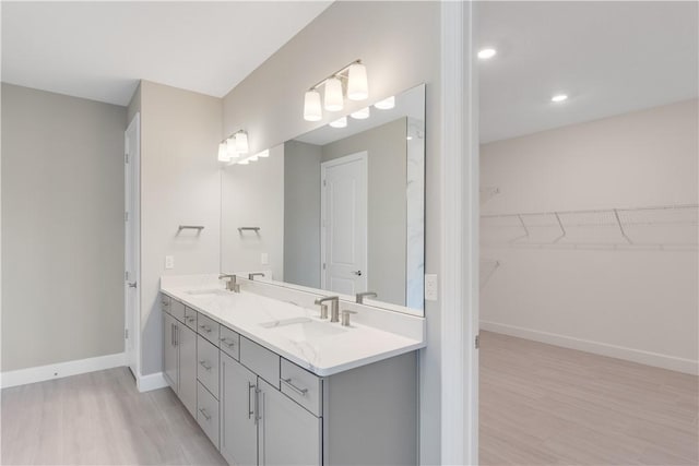 full bathroom with double vanity, wood finished floors, a sink, and baseboards