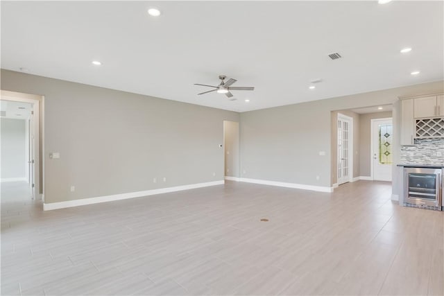 unfurnished living room with a bar, baseboards, wine cooler, and visible vents