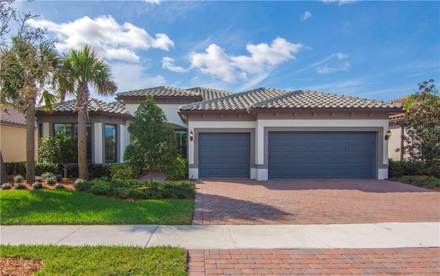 mediterranean / spanish house with a tiled roof, decorative driveway, an attached garage, and stucco siding