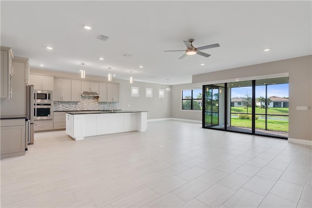 kitchen with dark countertops, an island with sink, appliances with stainless steel finishes, open floor plan, and a sink