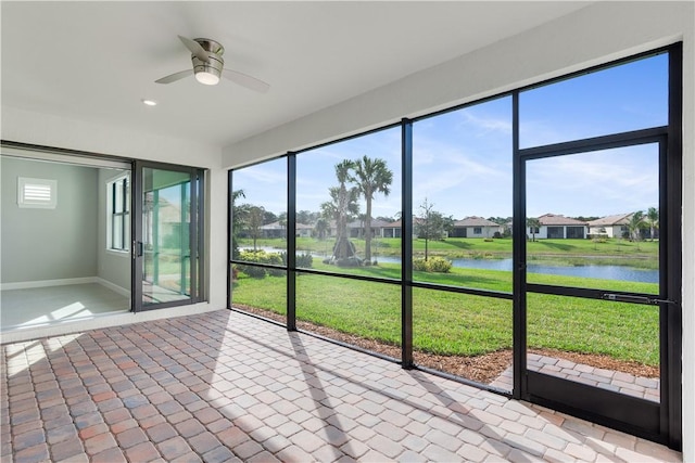 unfurnished sunroom featuring a ceiling fan, a residential view, a wealth of natural light, and a water view