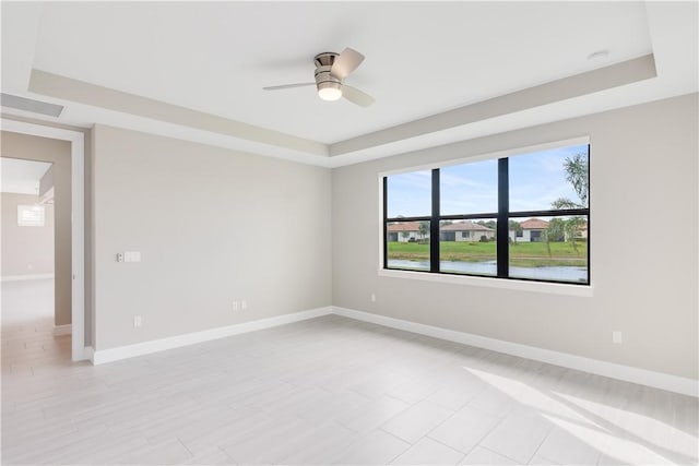 unfurnished room with a tray ceiling, a water view, ceiling fan, and baseboards