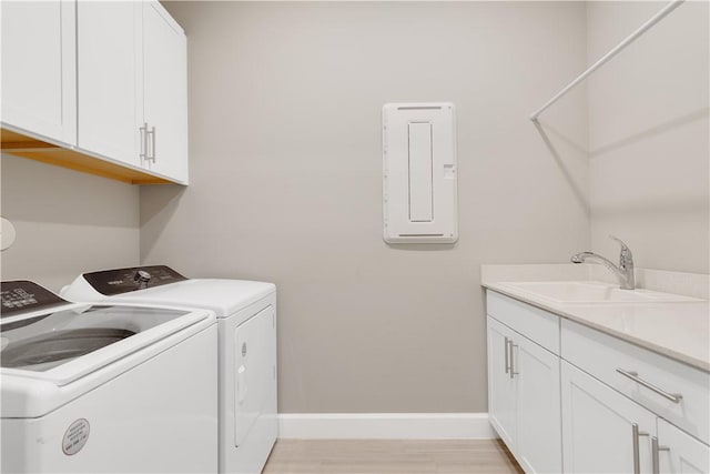 clothes washing area with light wood finished floors, cabinet space, a sink, separate washer and dryer, and baseboards