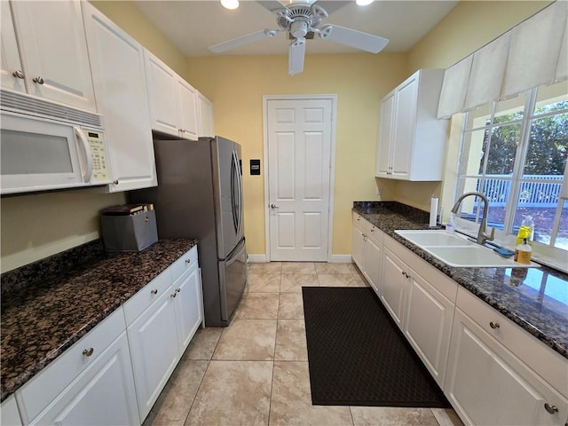 kitchen featuring sink, dark stone countertops, light tile patterned floors, white cabinetry, and stainless steel refrigerator