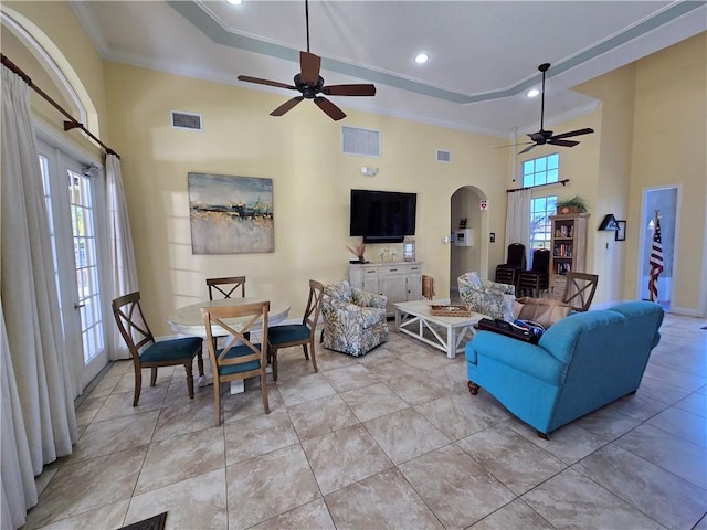 living room featuring a towering ceiling, a raised ceiling, ceiling fan, and crown molding