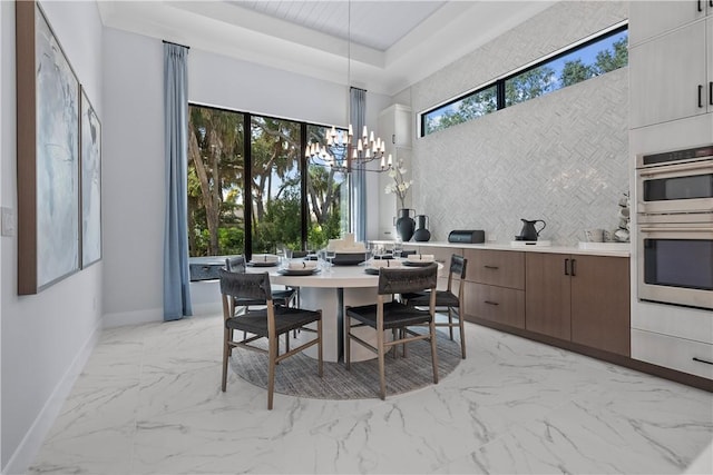 9259 Seaglass Ct, Vero Beach, FL 32963 - dining room featuring light marble finish floors, a chandelier, baseboards, a towering ceiling, and a raised ceiling