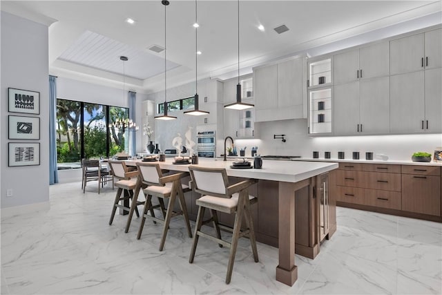 9259 Seaglass Ct, Vero Beach, FL 32963 - kitchen featuring a large island with sink, a breakfast bar, light countertops, glass insert cabinets, and light marble finish floors