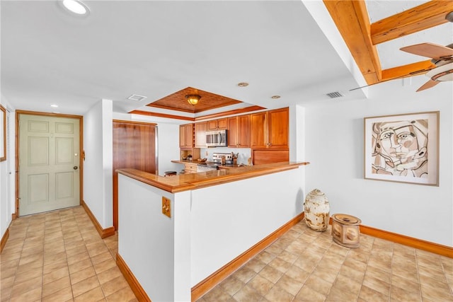 kitchen featuring brown cabinets, recessed lighting, stainless steel appliances, a tray ceiling, and baseboards