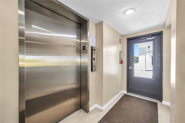 doorway with elevator, baseboards, and light tile patterned floors