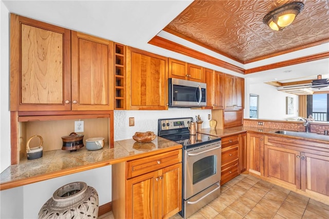 kitchen with stainless steel appliances, a sink, brown cabinetry, tile countertops, and a raised ceiling