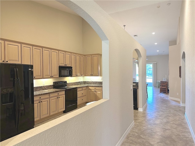 kitchen with a towering ceiling, light brown cabinetry, light tile patterned flooring, and black appliances