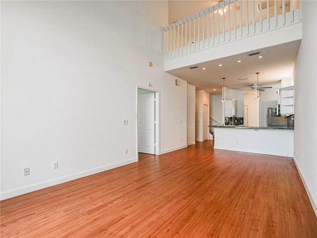 unfurnished living room with ceiling fan, a towering ceiling, and light wood-type flooring