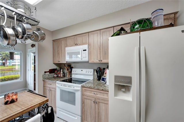 kitchen with a textured ceiling, light brown cabinetry, white appliances, and light stone countertops