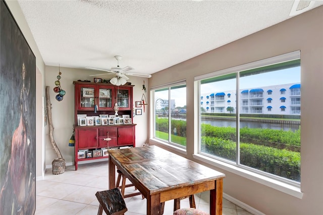 tiled dining area with ceiling fan, a textured ceiling, and a water view