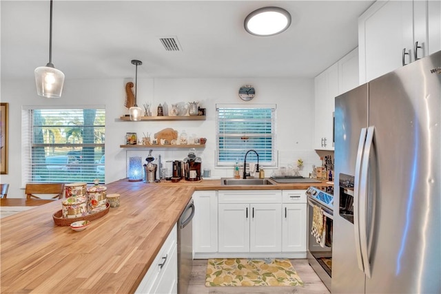 kitchen with sink, white cabinetry, butcher block countertops, pendant lighting, and appliances with stainless steel finishes