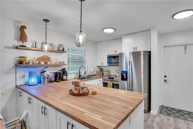 kitchen with hanging light fixtures, stainless steel appliances, wood counters, white cabinets, and sink