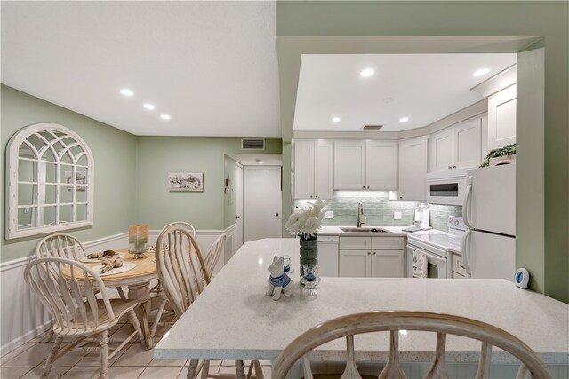 kitchen featuring tasteful backsplash, white cabinetry, light tile patterned floors, sink, and white appliances