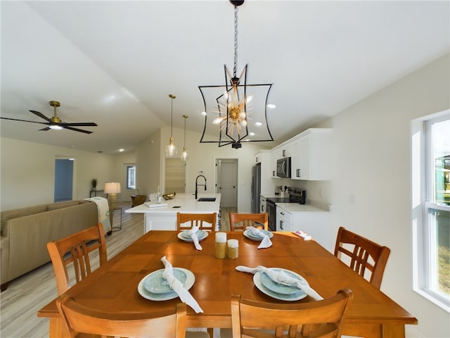 dining space with light wood-type flooring, ceiling fan with notable chandelier, and vaulted ceiling