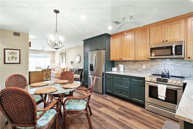 kitchen featuring ceiling fan with notable chandelier, hardwood / wood-style floors, hanging light fixtures, tasteful backsplash, and appliances with stainless steel finishes