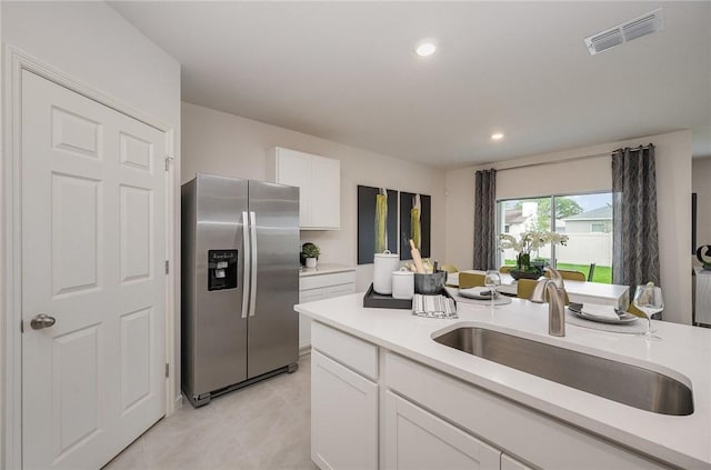 kitchen with stainless steel fridge, visible vents, light countertops, white cabinetry, and a sink