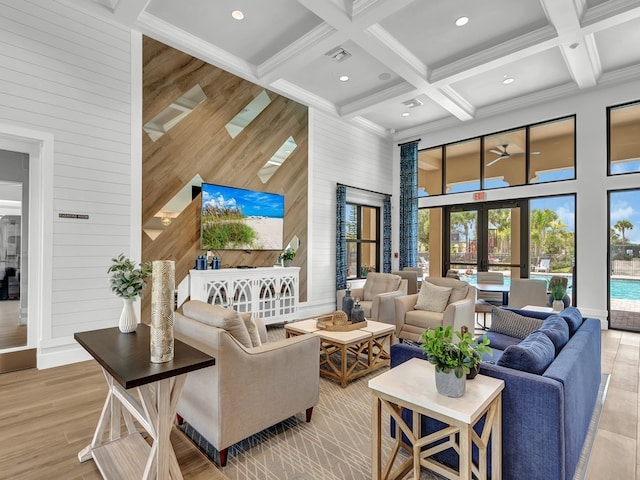 living room with coffered ceiling, a towering ceiling, wood walls, and french doors