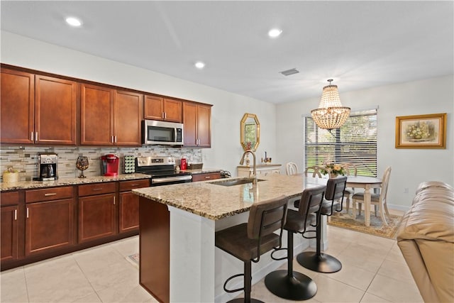 kitchen with sink, light tile patterned floors, stainless steel appliances, light stone countertops, and an island with sink