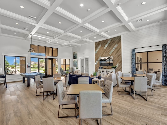 dining space with beamed ceiling, a towering ceiling, and light hardwood / wood-style floors