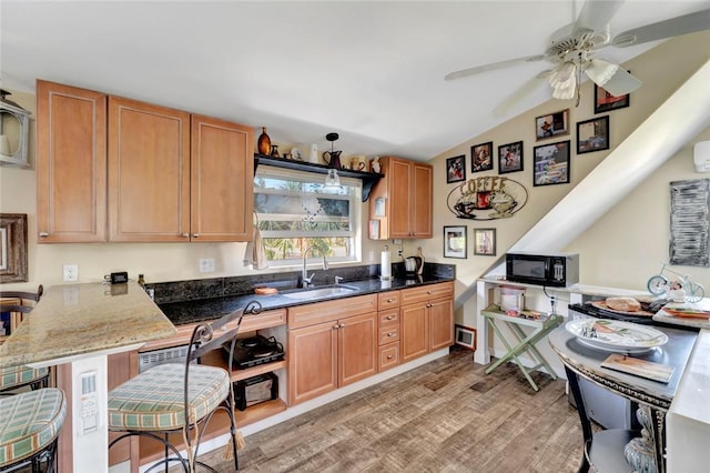 kitchen featuring vaulted ceiling, sink, dark stone counters, light hardwood / wood-style floors, and kitchen peninsula