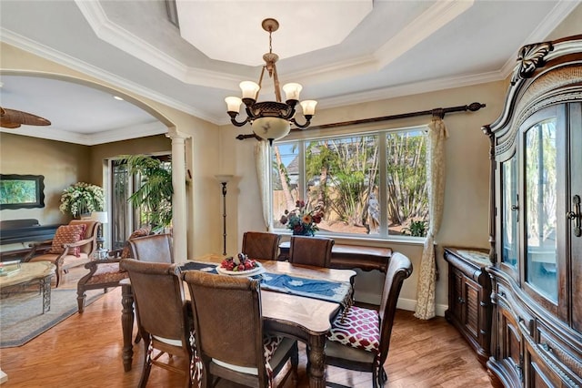 dining space with an inviting chandelier, light wood-type flooring, and a tray ceiling