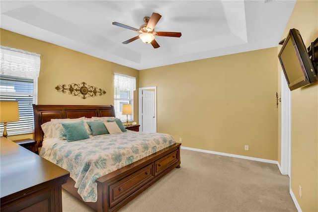 bedroom with ceiling fan, light colored carpet, and a tray ceiling