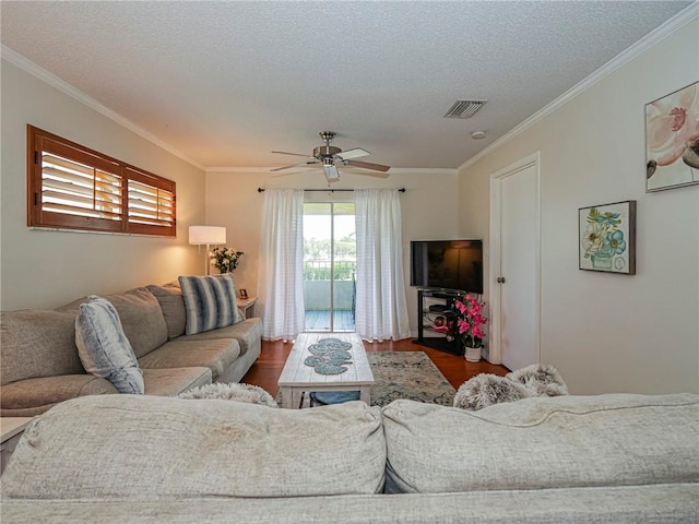 living area featuring wood finished floors, visible vents, a ceiling fan, crown molding, and a textured ceiling