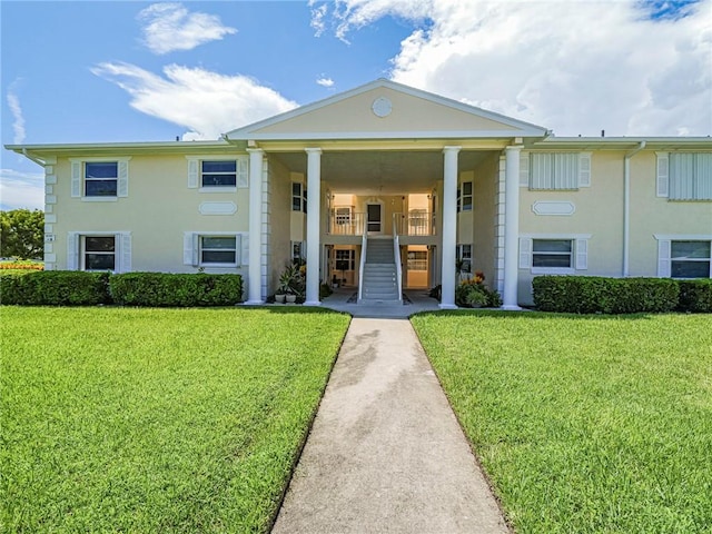 view of front facade featuring stairway, a front yard, and stucco siding