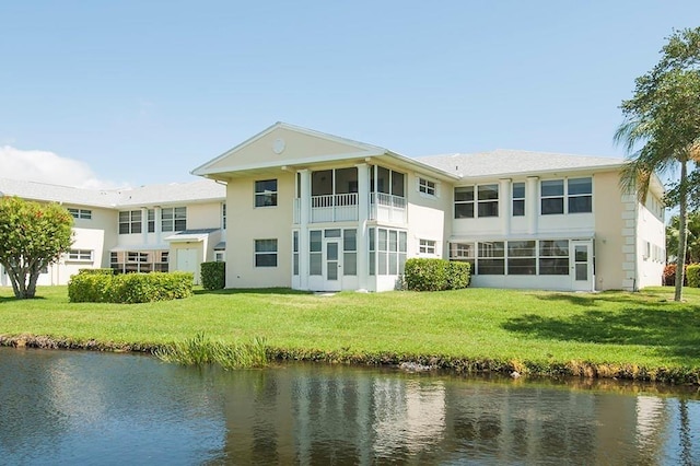 rear view of property featuring a lawn, a water view, and stucco siding
