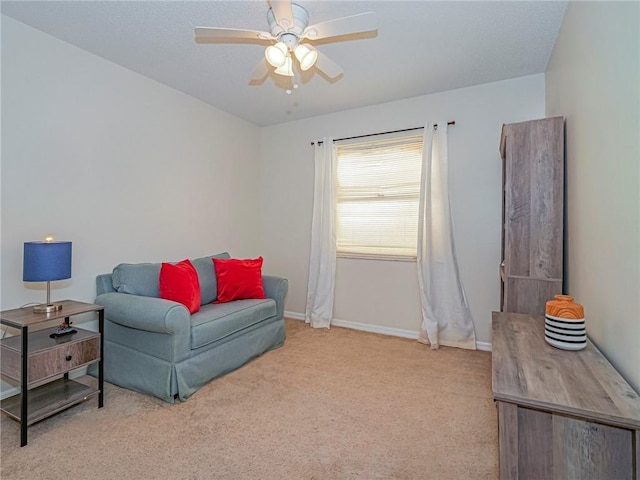 living area with a ceiling fan, baseboards, and light colored carpet